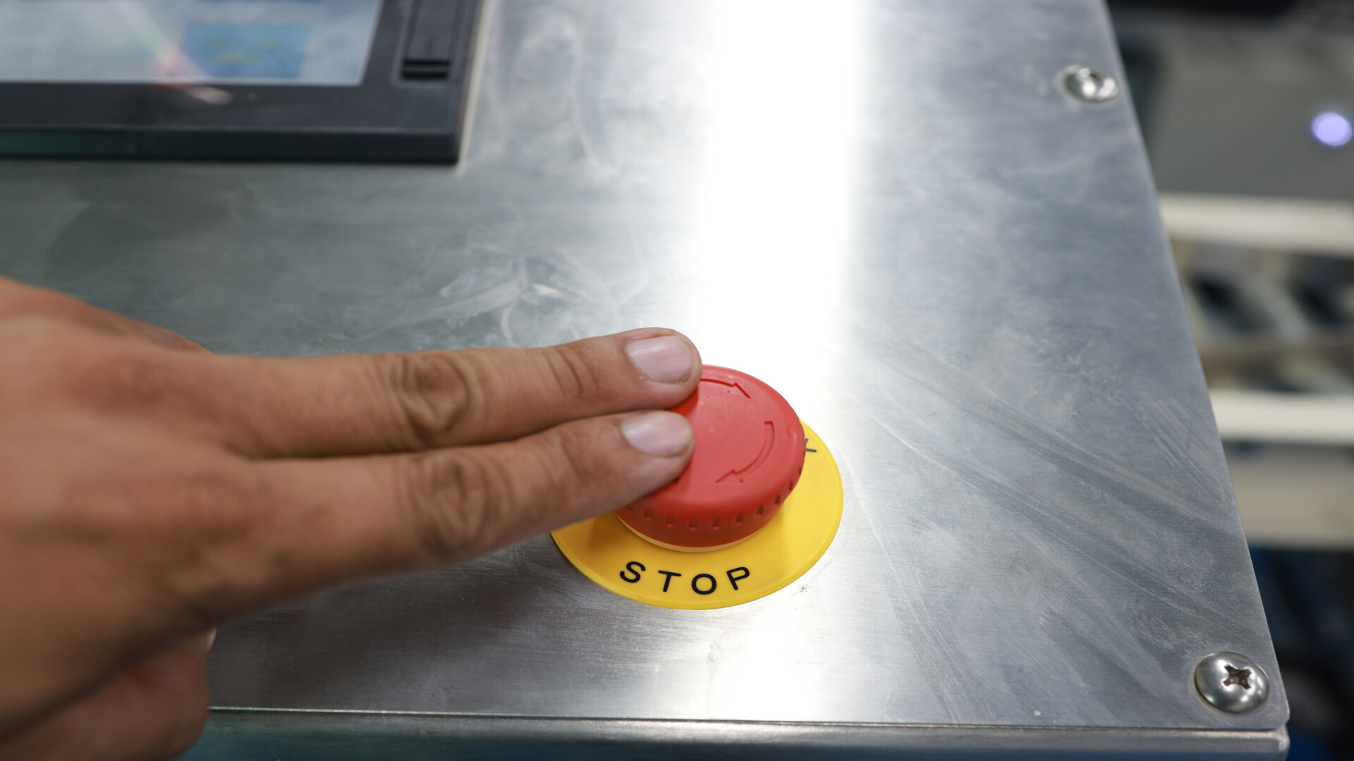 A hand presses the red emergency stop button of an industrial machine. A visual metaphor for a switch that halts the execution of code: exactly what zend.disable_eval does for eval().