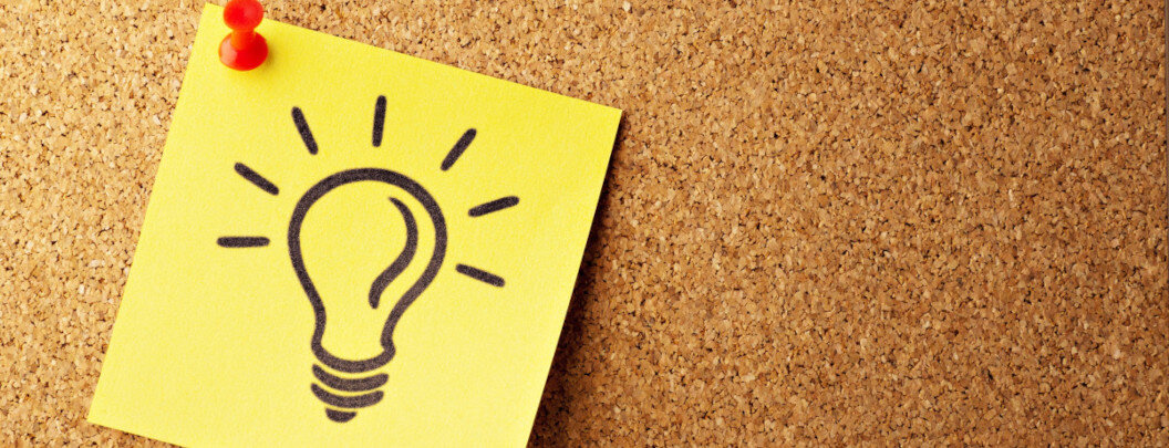 The image shows a cork notice board with a yellow sticky note attached to it with two red pins. The note has a stylised light bulb drawn on it, representing an idea or a flash of inspiration. The light bulb is surrounded by short lines symbolising rays of light, reinforcing the image of creative inspiration or a brainwave.