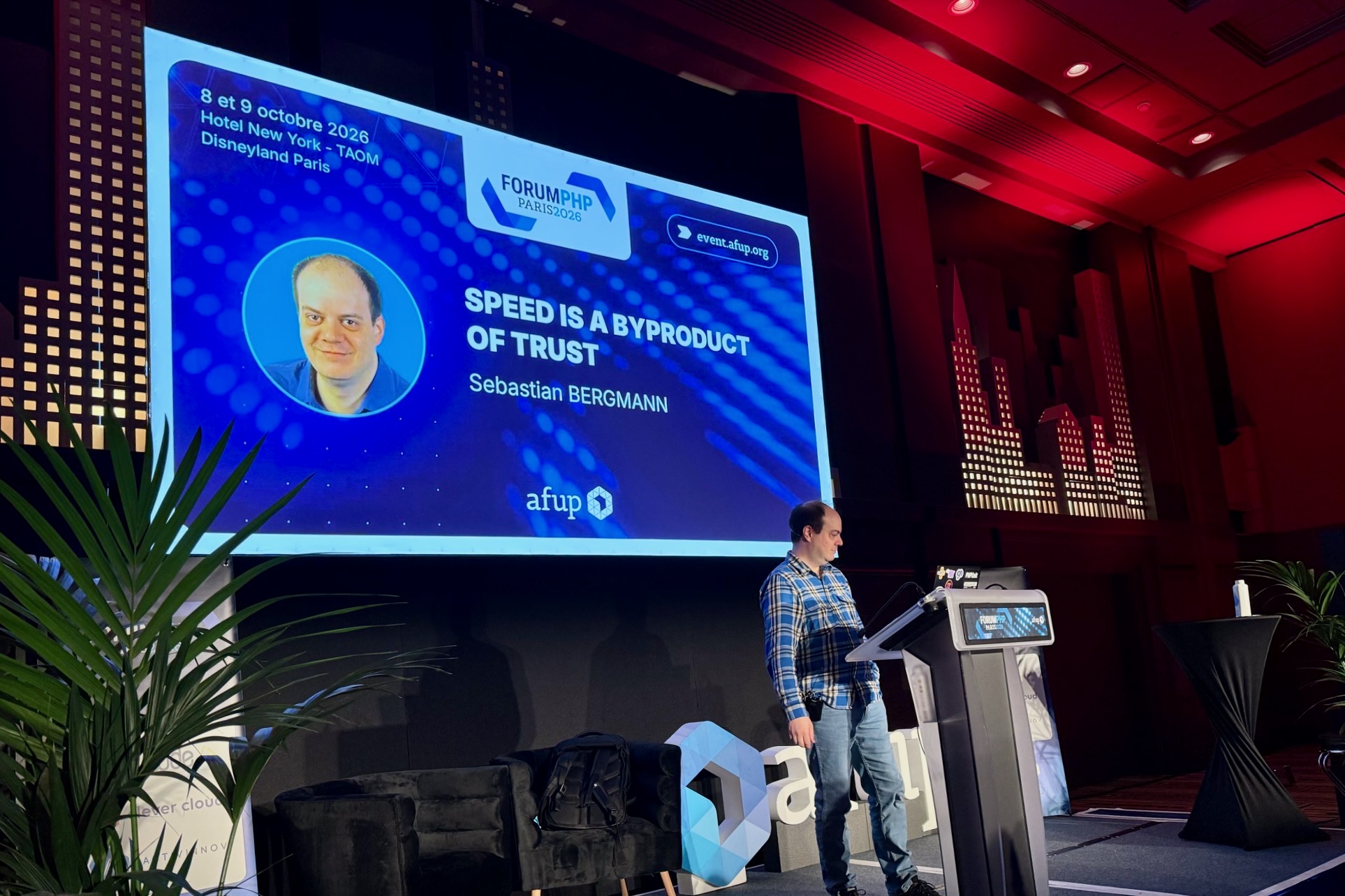 Sebastian Bergmann at the lectern at Forum PHP 2026. The screen behind him announces his talk “Speed is a byproduct of trust”.